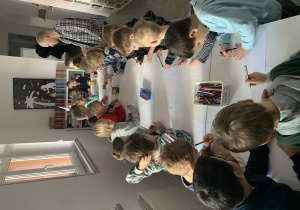 Dzieci tworzą ilustracje do książki pt. "Zmartwiozaur" czytanej przez pracownika biblioteki